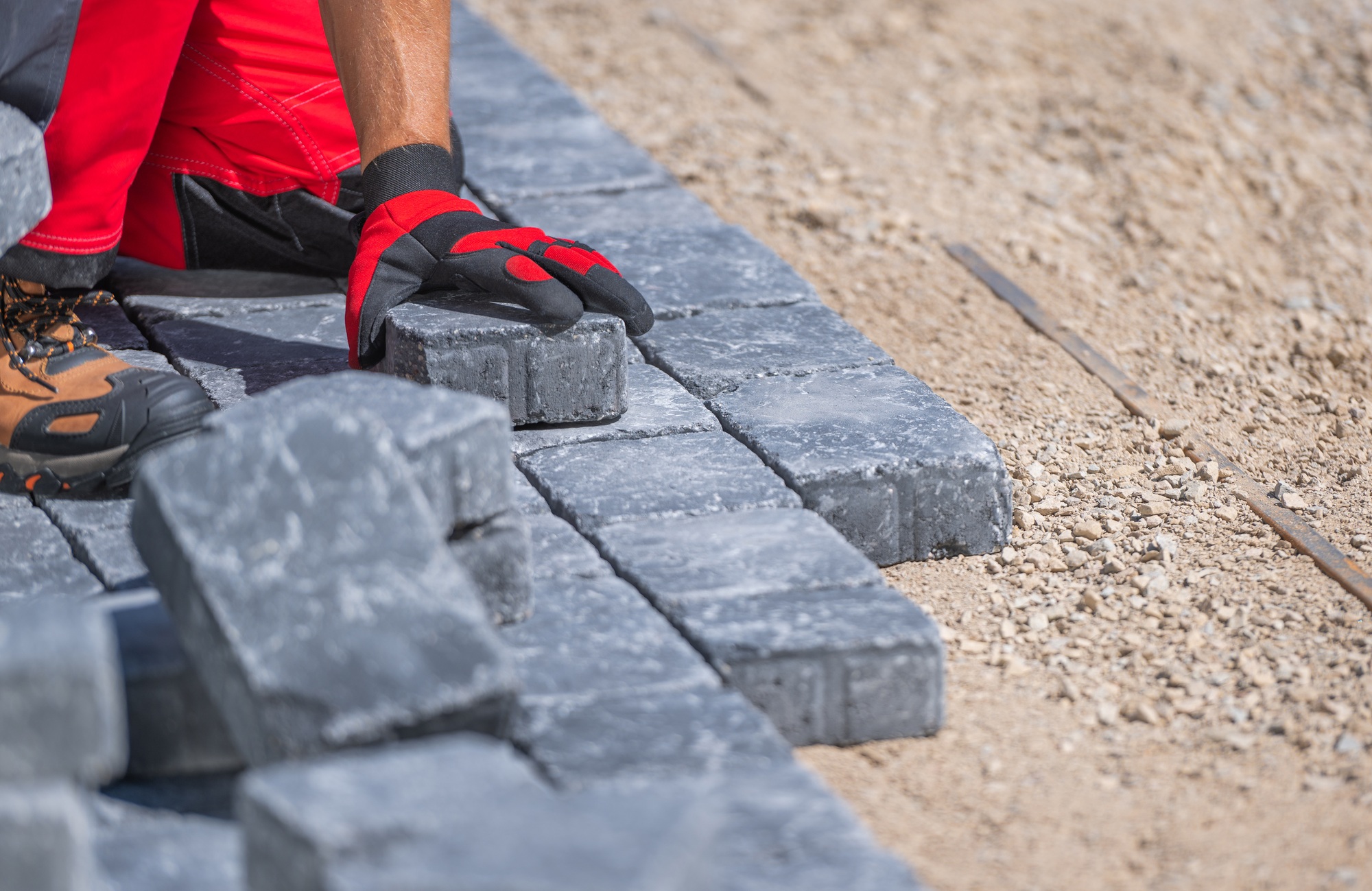 Worker Laying Grey Pavers on a Construction Site During Daytime for Outdoor Pathway Installation