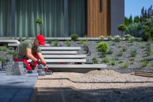 Worker Laying Stone Pavers in a Landscaped Yard During a Sunny Afternoon